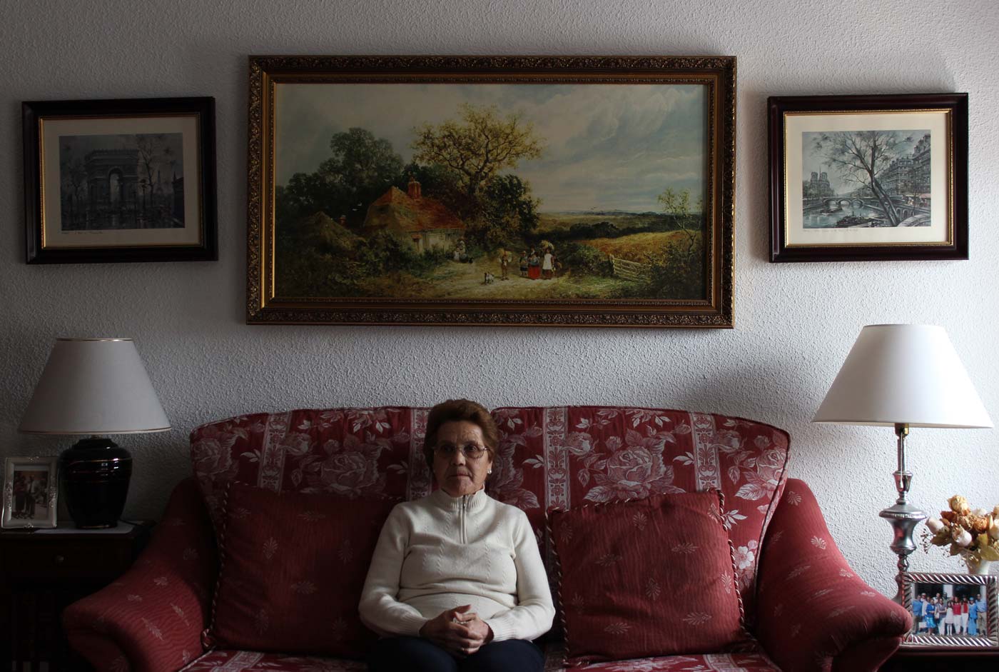 Persona mayor sentada en el sofá de su casa con cuadros y pinturas en la pared. | Fotografía de Eduardo Oyana